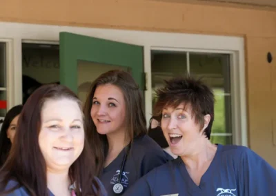 Three smiling veterinary staff members in scrubs stand outside Adobe Veterinary Center.