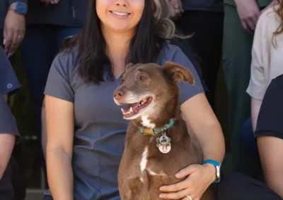 Smiling woman in scrubs holding a brown dog with a blue collar outside with a team.